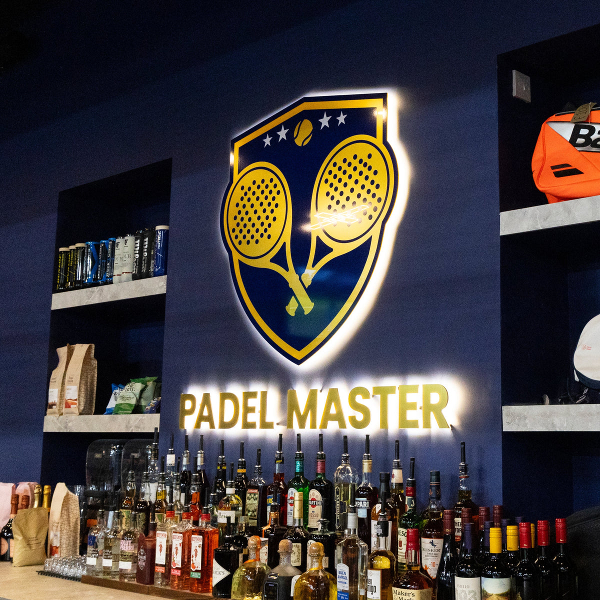 A retail display featuring a large illuminated 'PADEL MASTER' sign on a dark blue wall